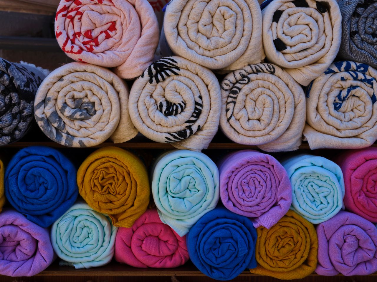 Colorful rolled towels neatly arranged on wooden shelves, showcasing vibrant textile design.