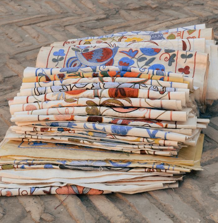 A vibrant stack of embroidered textiles displayed on a stone surface in Khiva, Uzbekistan.