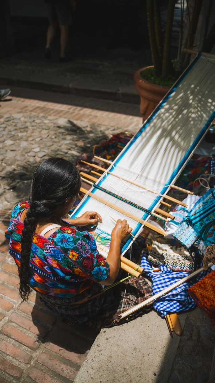 A woman weaves vibrant textiles outdoors in Antigua Guatemala.