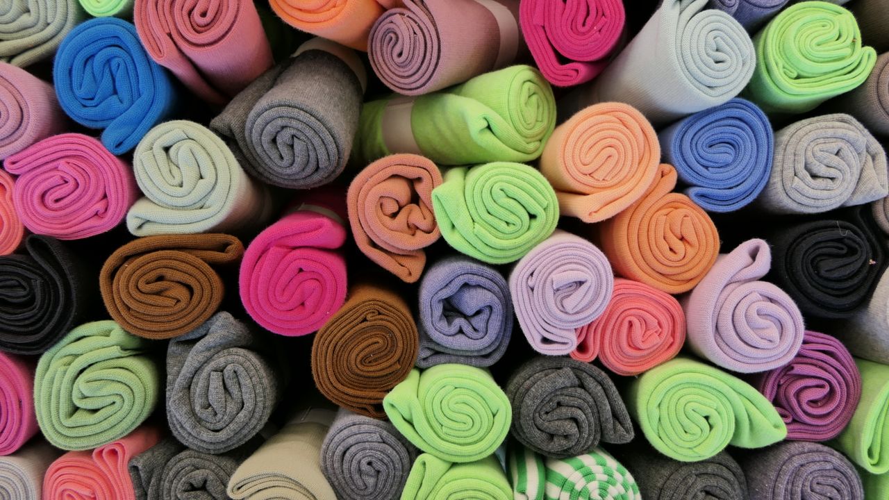 Vibrant rolls of fabric arranged neatly, showcasing a rainbow of colors.